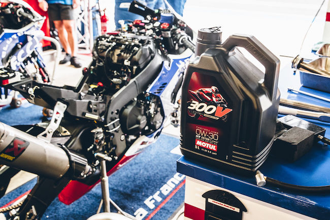 A View of the Motul 300V Factory Line Racing Kit Oil 2376H 0W-30 ESTER Core® next to a Honda Racebike