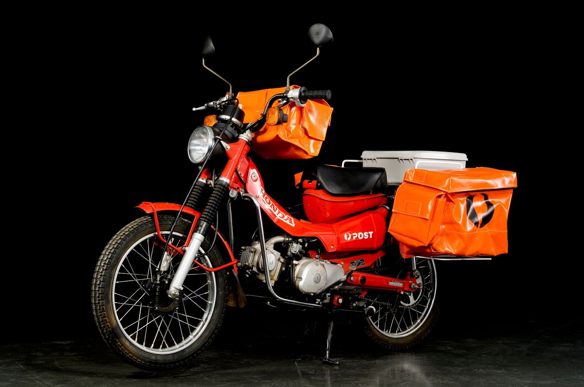 A Honda CT110 'Postie' bike with mailbags in a studio