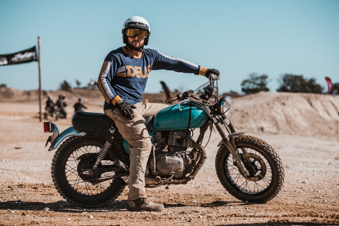 A man on a dirty off-road motorcycle poses for the camera