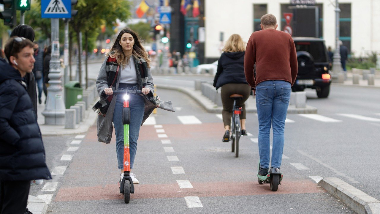 A man and a woman on electric scooters share the bike lane with a woman on a normal bicycle.