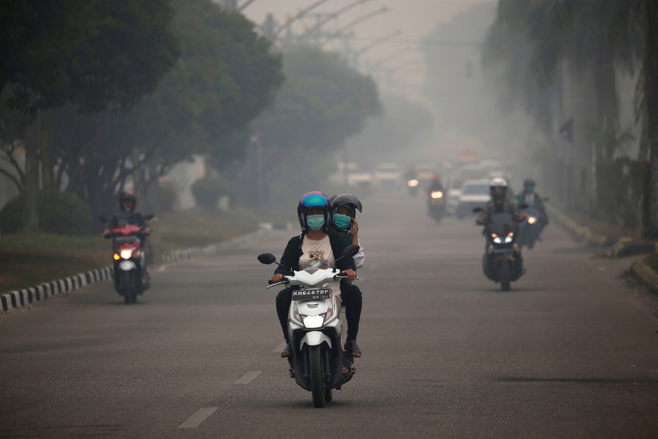 An image of a rider and pillion on a moped riding through smog in a city.